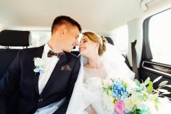 Close-up portrait of newlyweds kissing in the back seat of a car.